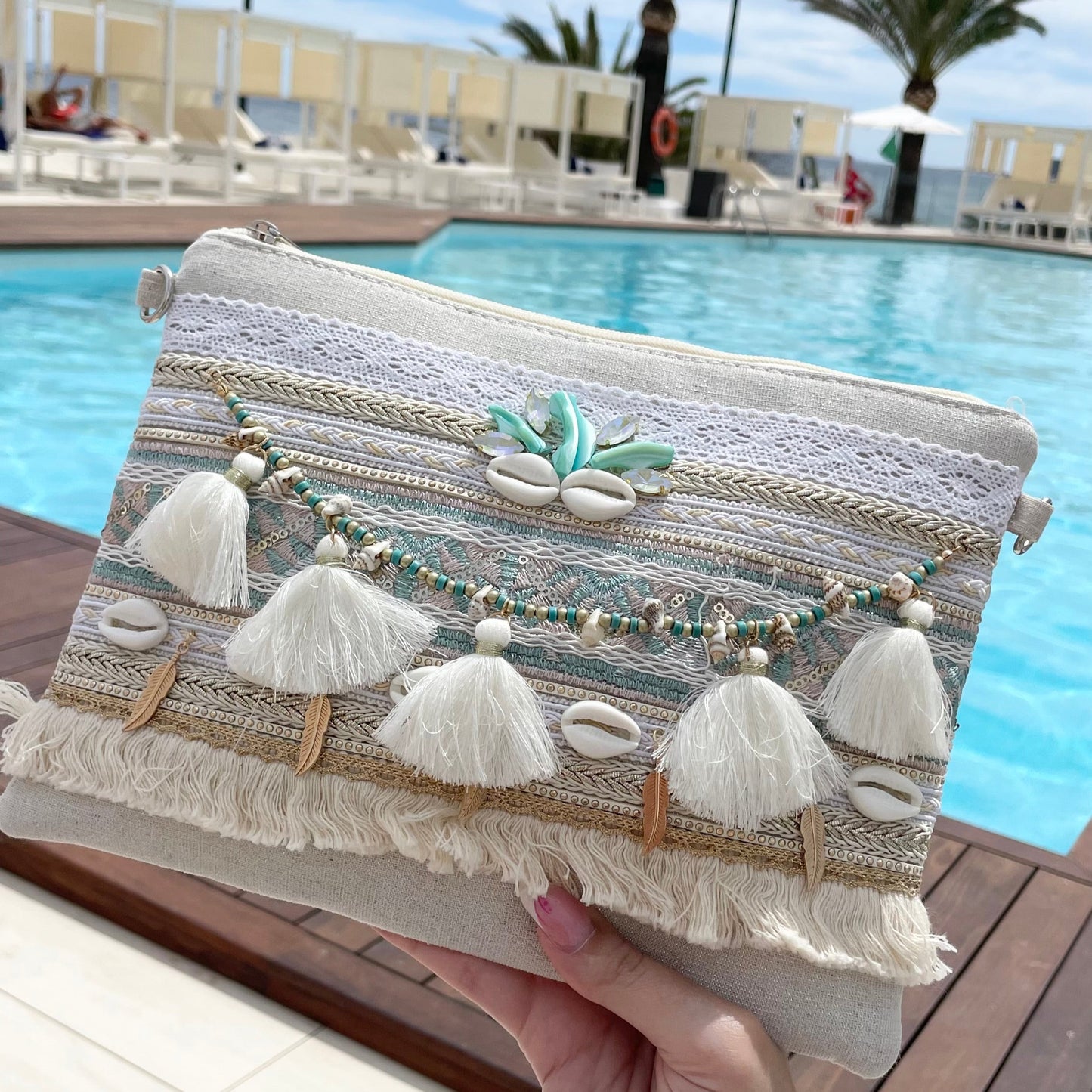 Pochette bleu bohème chic en tissu décorée de dentelle ajourée, tresse ethnique, pompons, perles bleues, plumes et coquillages – accessoire mode été femme Collection Ibiza avec bandoulière réglable